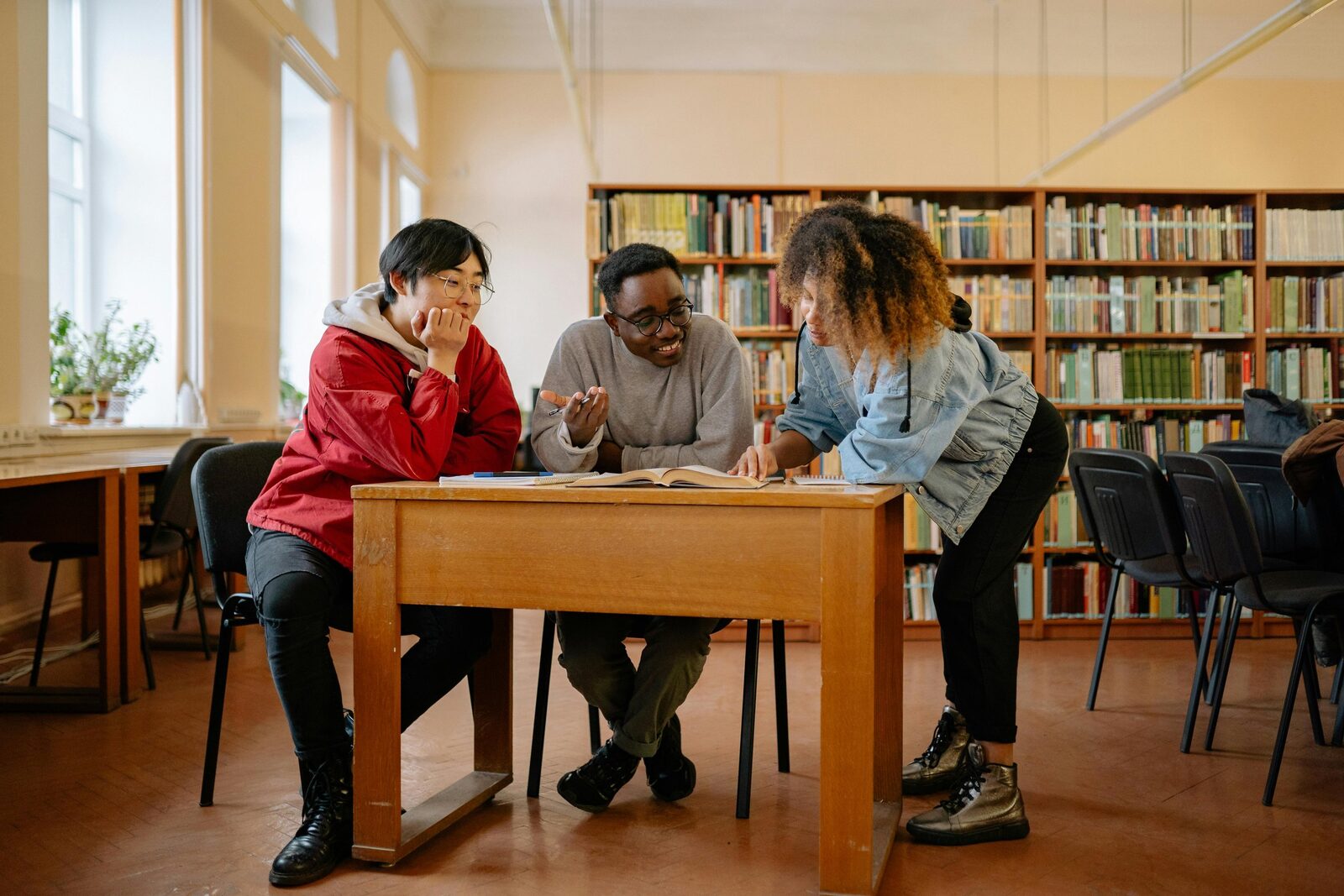 A teacher and student sit at facing desks in an otherwise empty classroom, sharing an apple.