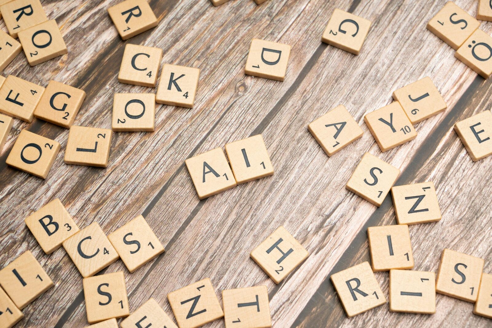 A mix of wooden scrabble-style letters rest on a wooden table top; in the center, the tiles 'AI' are featured.